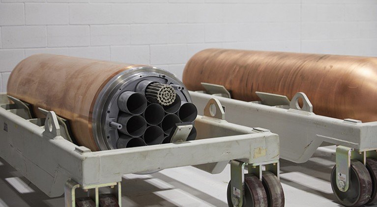 Two cylindrical copper fuel containers displayed in a white room.