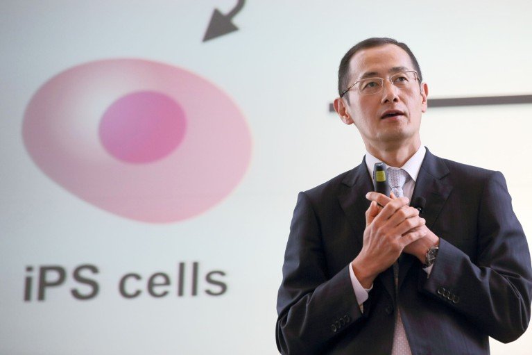 Shinya Yamanaka gives a talk in front of a screen displaying an iPS cell