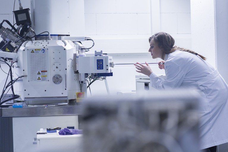 A scientist uses a scanning electron microscope in a laboratory filled with research equipment.