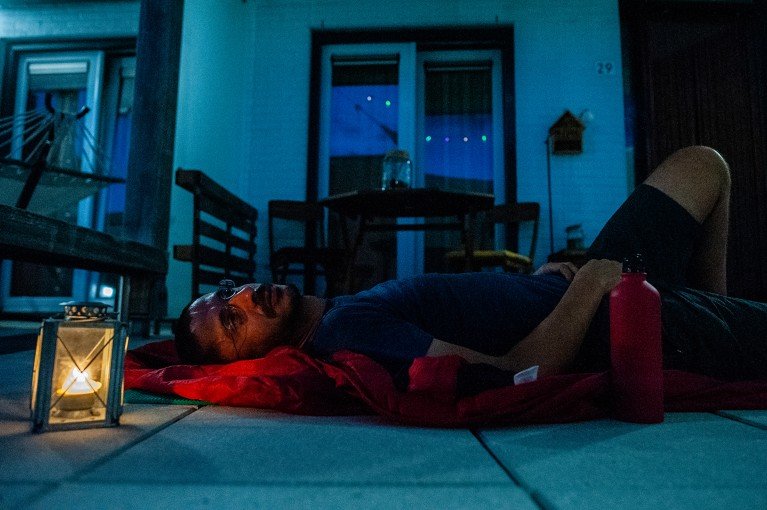 A man sleeps on a terrace during a heatwave in the Netherlands, resting on a mat beside a small lantern at night.