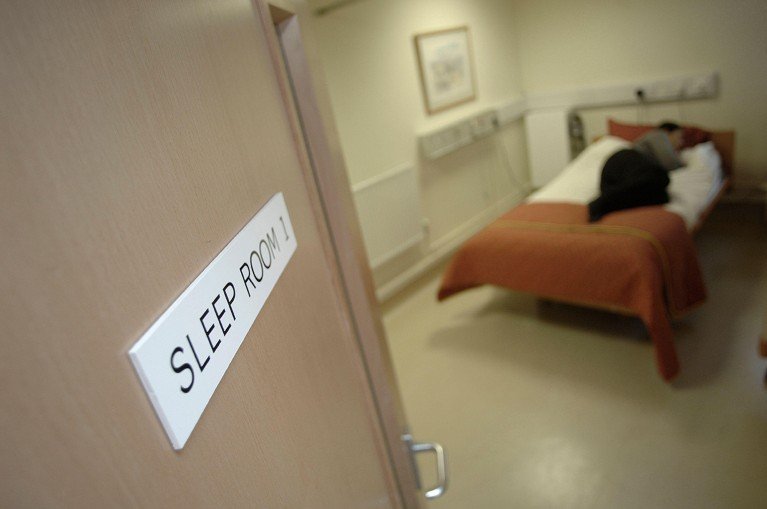A patient sleeps in a bed, viewed through an open doorway at a sleep clinic.