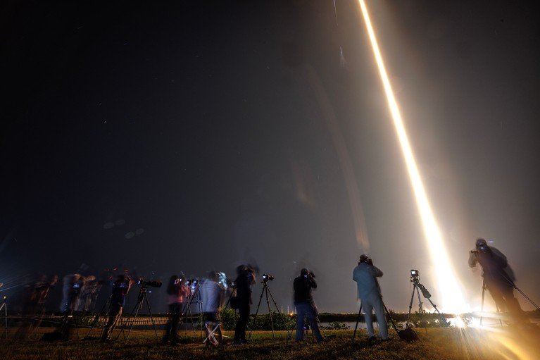 People take photos of a SpaceX rocket lifting off.