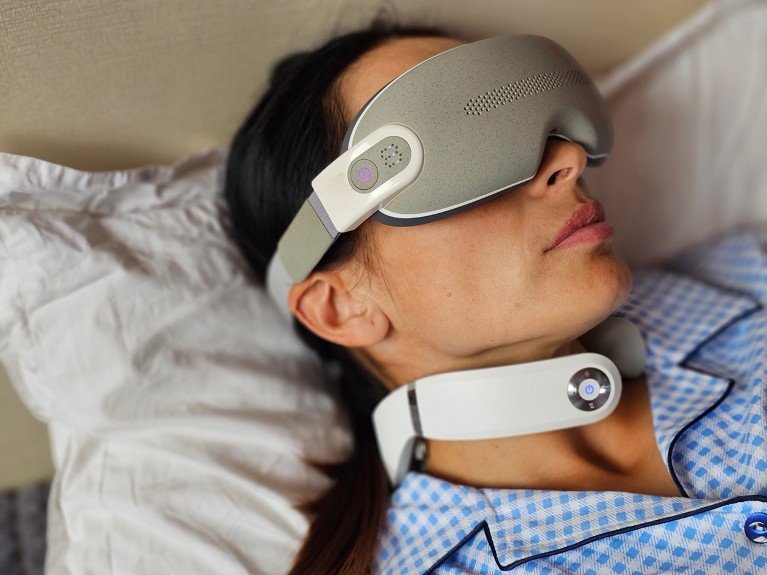 A person wears an eye mask and neckband in bed.