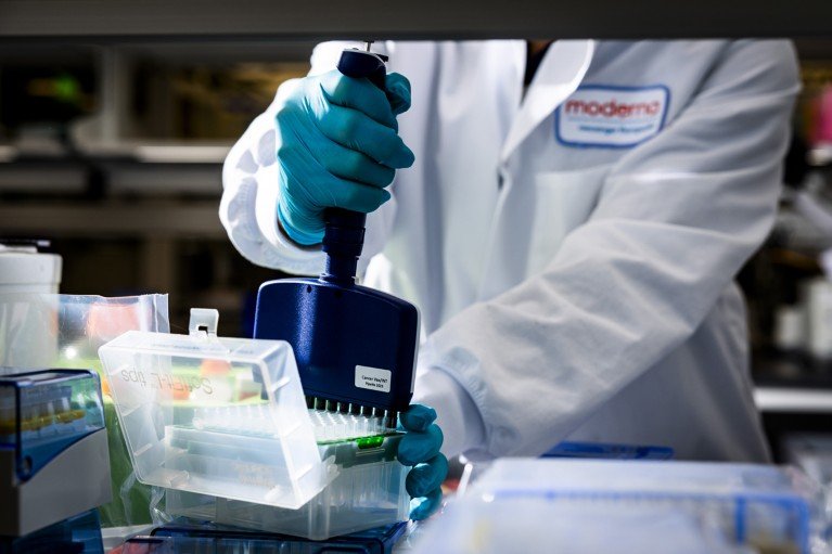 Close-up of a laboratory researcher wearing blue gloves and a white lab coat conducting cancer vaccine research