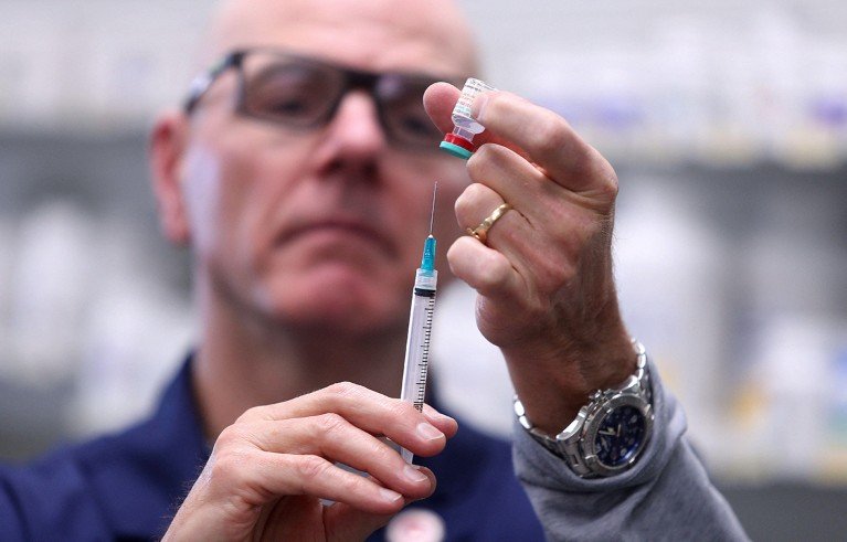 A person preparing a syringe with a vaccine vial, focusing on hands holding the syringe and vial. Background is blurred, highlighting careful medical procedure and vaccine administration.