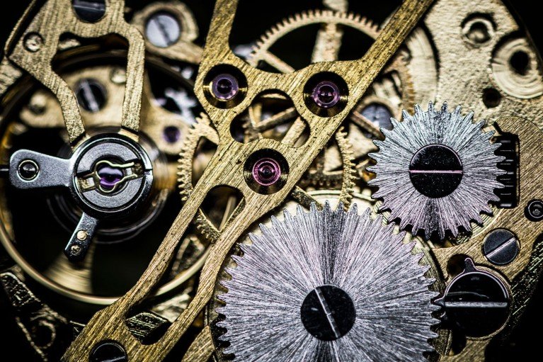 A close-up of gold and silver coloured interlocking gears and components inside a mechanical clock.