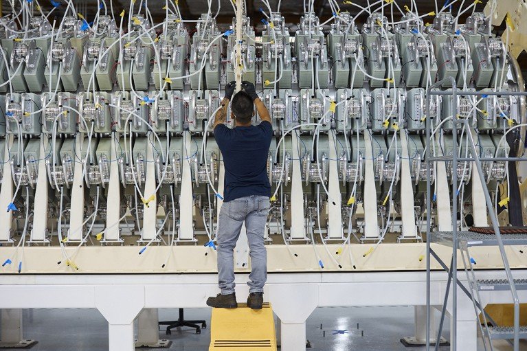 A technician wearing gloves stands on a stool assembling part of a truck-sized module that is part of Pacific Fusion’s machine.
