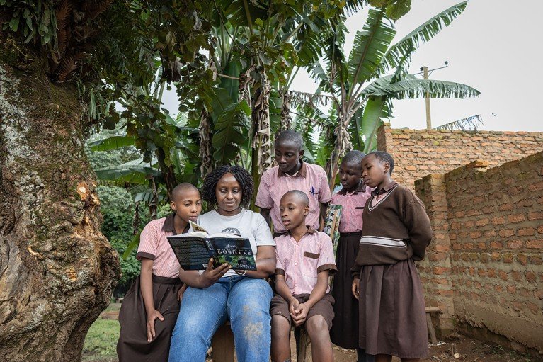 Gladys Kalema-Zikusoka reading a book that she has authored on gorillas to school children outside a school in Uganda.