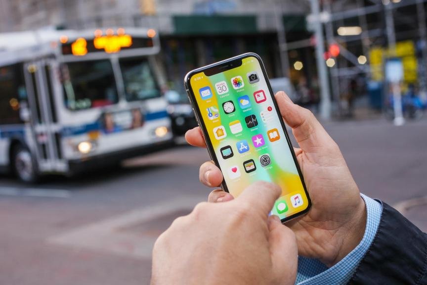 A person is holding up the iPhone X and using the touchscreen with their finger.