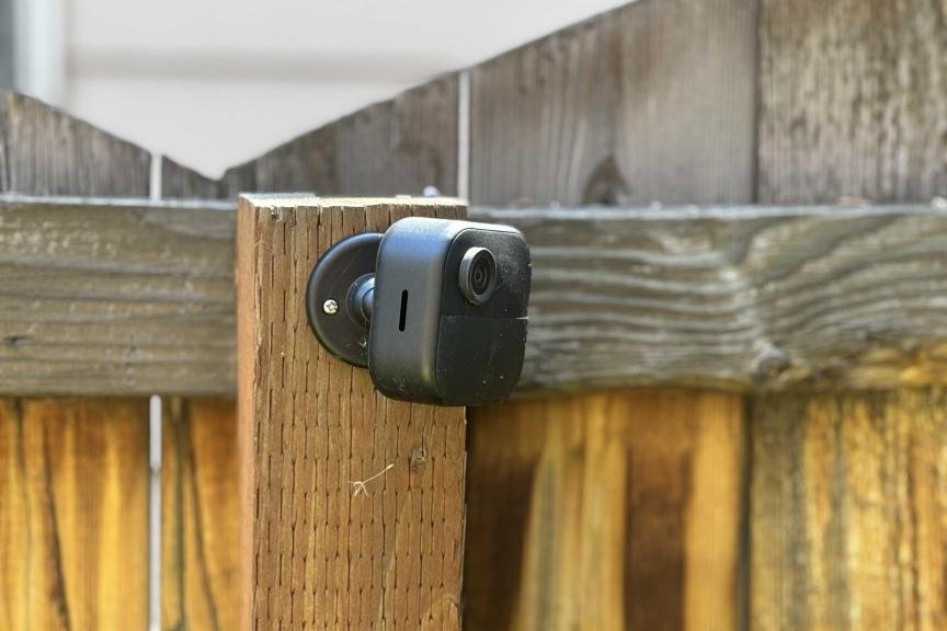 The Blink Outdoor 4, a small black square security camera, mounted on a wooden fence.