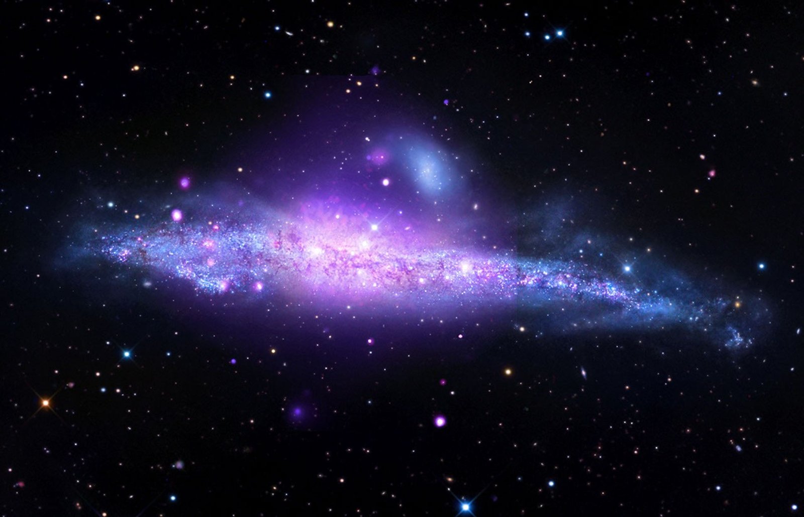 A spiral galaxy viewed from its side, featuring a giant halo of hot gas blowing out of its stellar disk. X-rays from Chandra and ESA’s XMM-Newton (purple and royal blue) trace hot gas driven out by supernovas and black holes and neutron stars pulling gas from their companions, while optical light (light blue, gold and white) from ground-based observer R. Jay GaBany showcases dense dust lanes. Edge-on views of galaxies allow astronomers to study how flat their stellar disks are and provide the clearest views of material located above or below the disk.