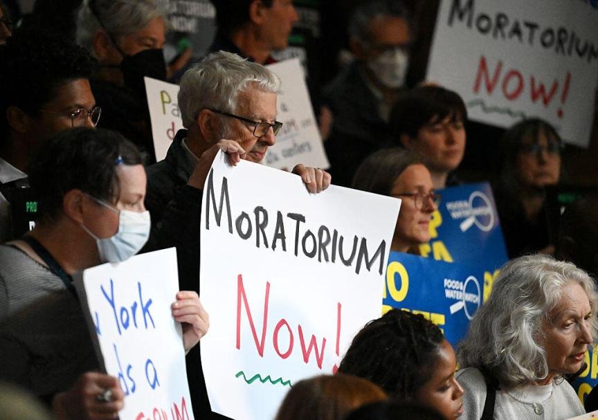 People hold up signs saying "Moratorium Now!" at an anti-AI data center rally in Albany, New York in May 2026.
