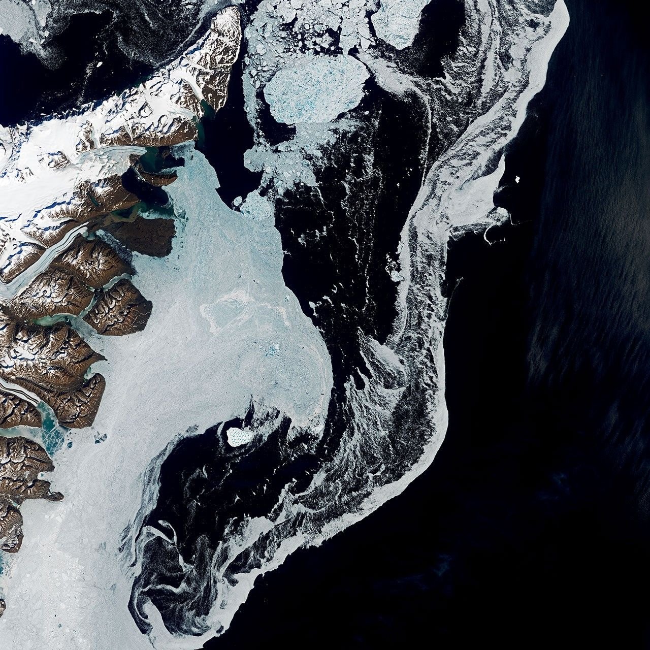 A satellite image shows the dark blue waters of the Denmark Strait with swirling sea ice to the right of eastern Greenland. A bright white iceberg sits amid the sea ice in the middle-left of the scene.