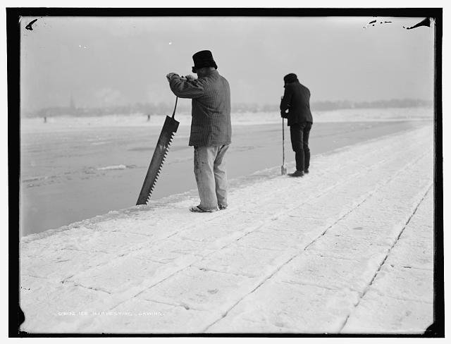 black and white photograph of two workers harvesting ice from a frozen lake.