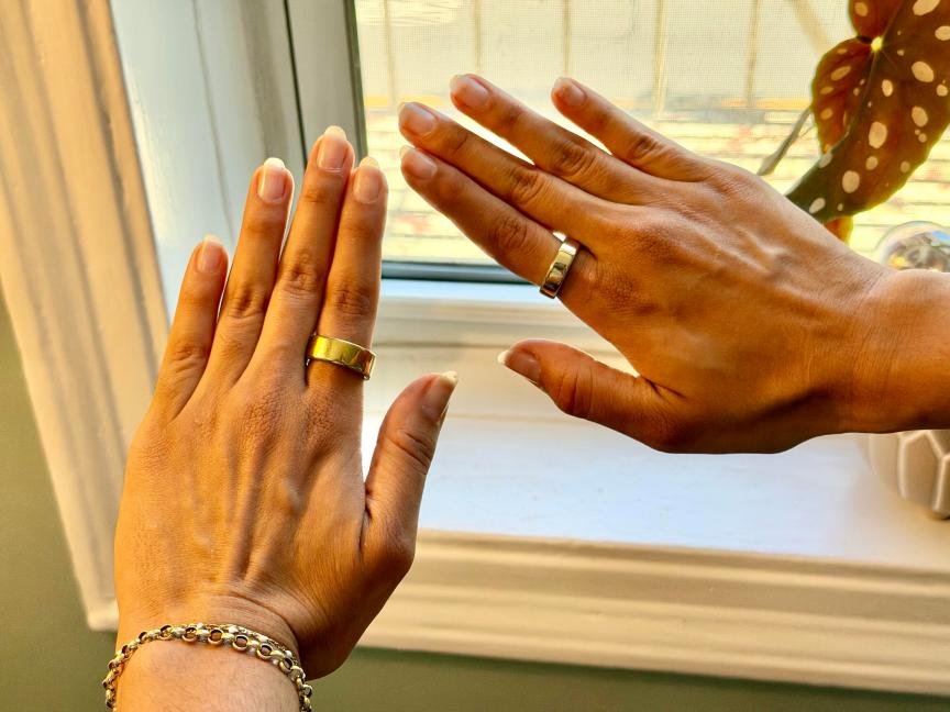 Two hands wearing smart rings on the pointer fingers. The Oura Ring 4 is on the left hand and the smaller Oura Ring 5 is on the right hand.