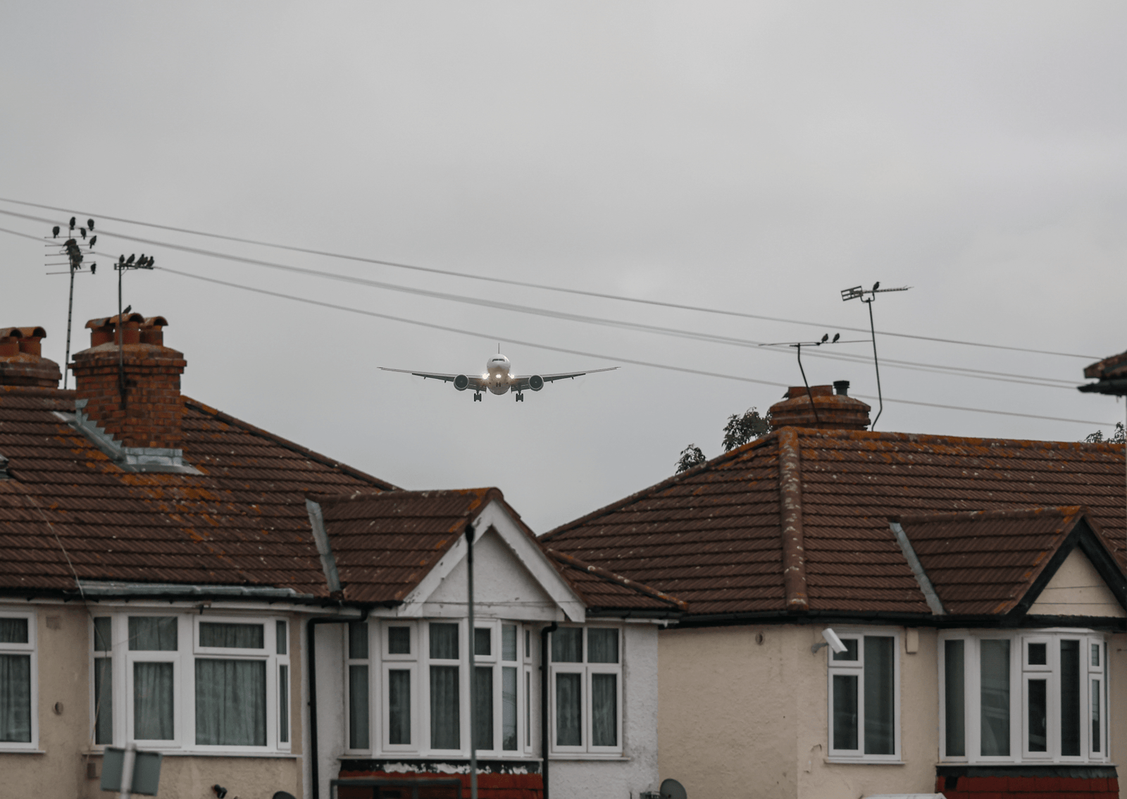a singapore airlines plane beginning its descent between two houses with red roofs