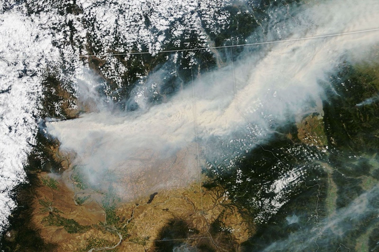A wide plume of brown-gray smoke stretches across a satellite image spanning Washington, Idaho, Montana, and Canada.
