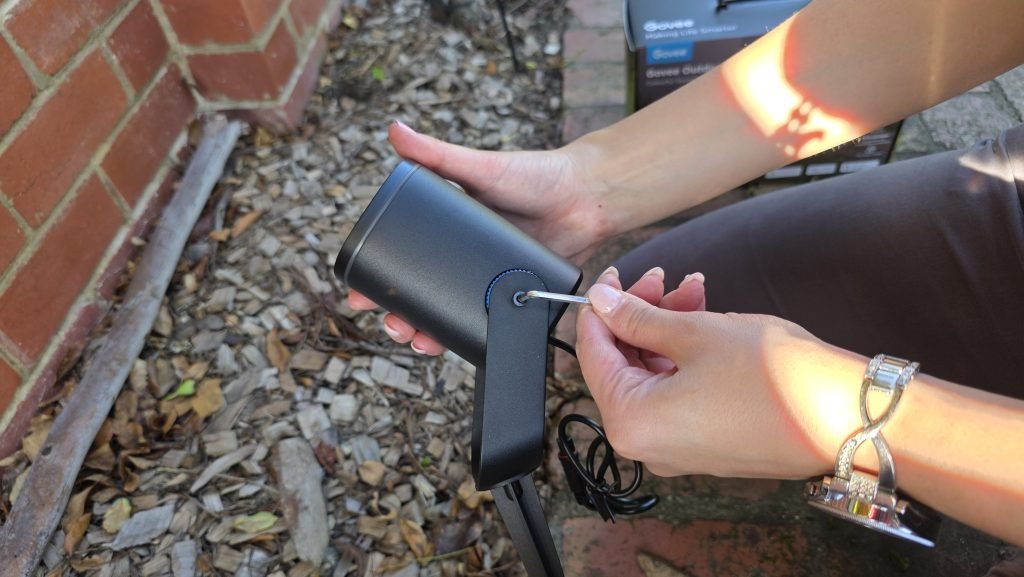 Adjusting the bracket on the Govee light using the Allen key and the exposed screw on the left side of the light. One hand holds the light whilst the other holds the allen key.