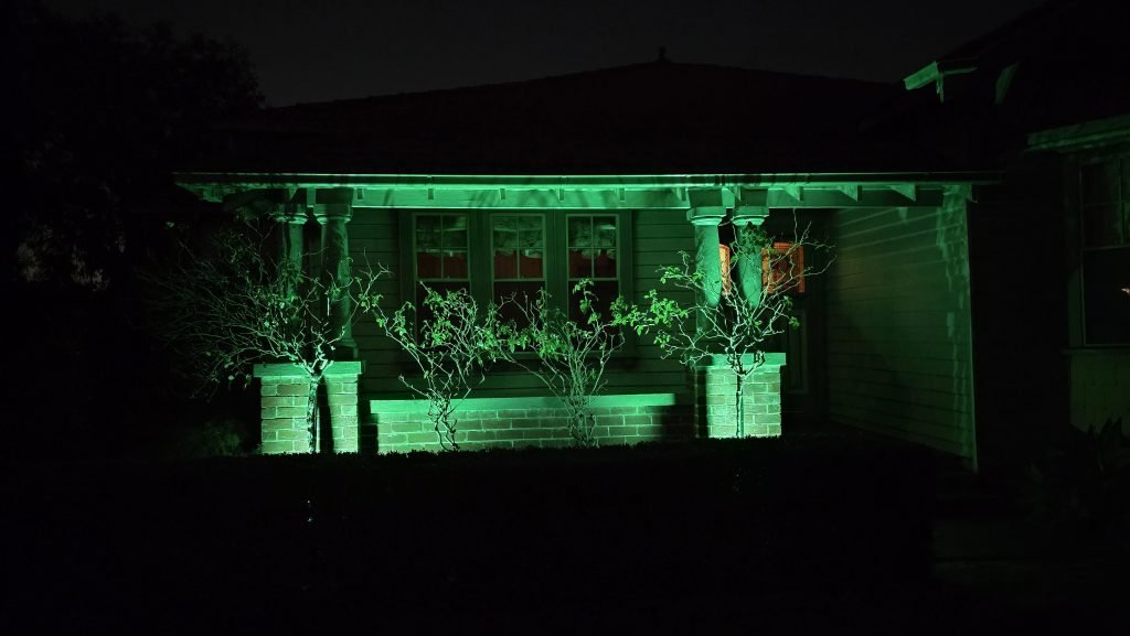 Photo of the lights lighting up four large rose bushes at the entrance to the house. The lighting colour is green.