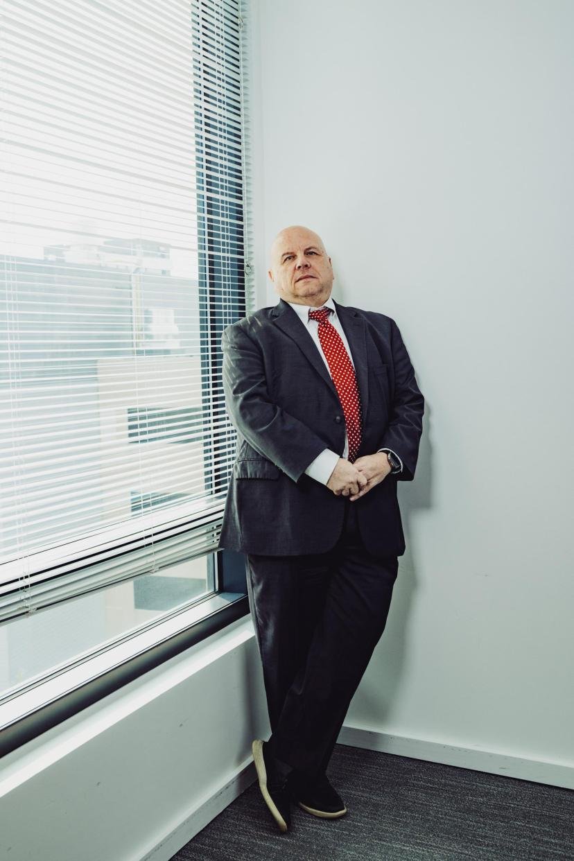 Buddy Rizer, an older man wearing a suit, poses for a portrait near the window in his office.