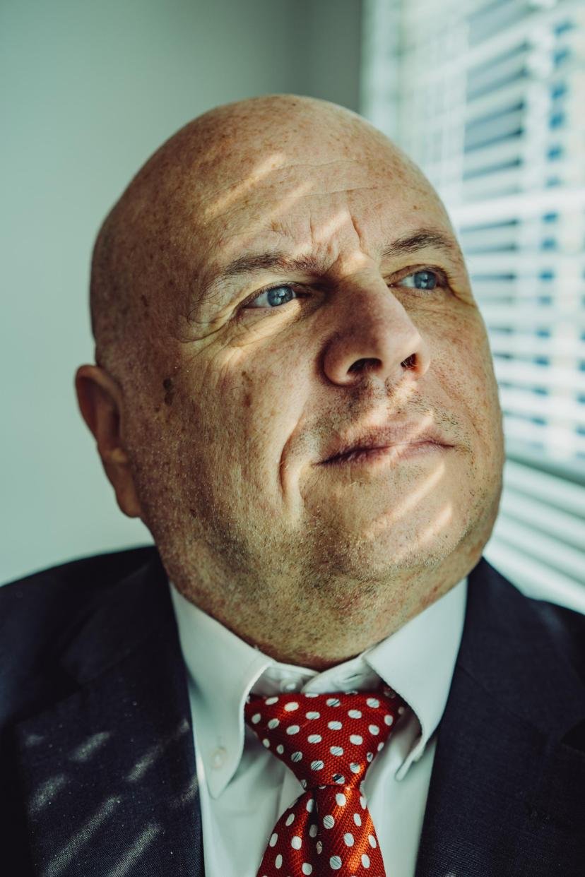 Buddy Rizer, an older man wearing a suit, poses for a portrait near the window in his office.