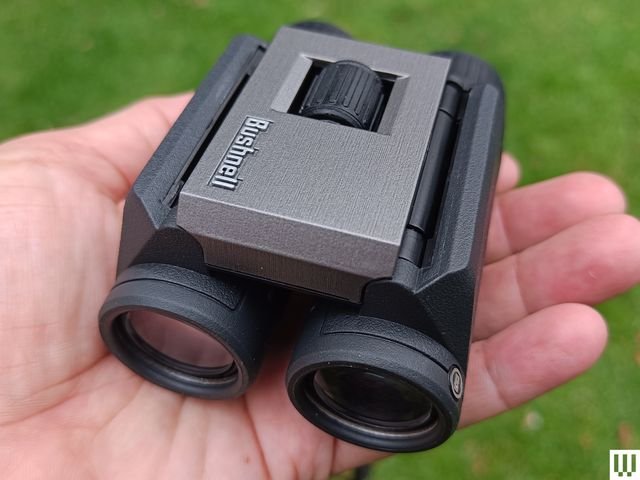 The Bushnell Powerview binoculars compactly folded in the palm of a person's hand, lenses facing inward.