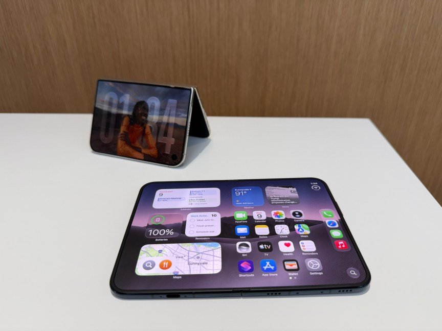 Two foldable phones on a table, one unfolded flat and one half-folded and upright like a tent.