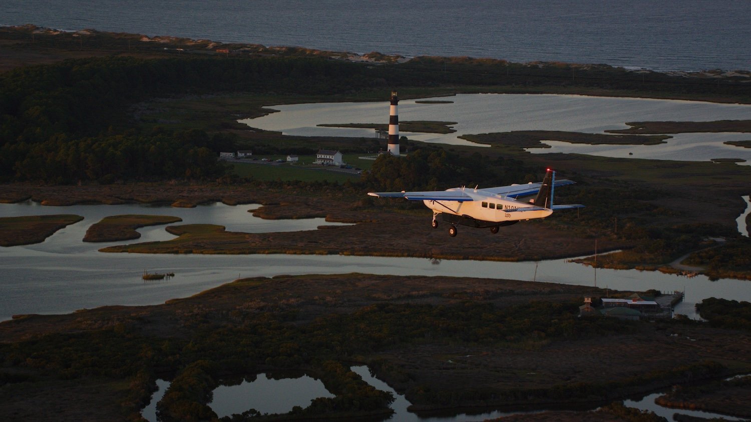 Cessna airplane flying above South Carolina coast with marshes and lighthouse beneath it