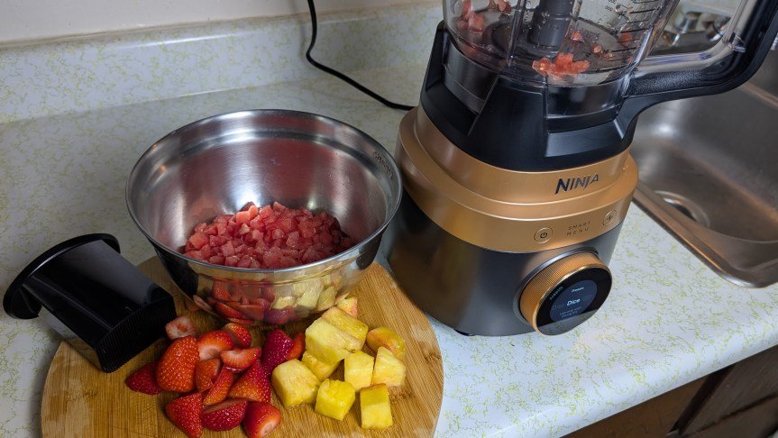 Ninja-CrushBoss-food-processor-next-to-bowl-of-diced-watermelon-and-fresh-fruit-on-cutting-board
