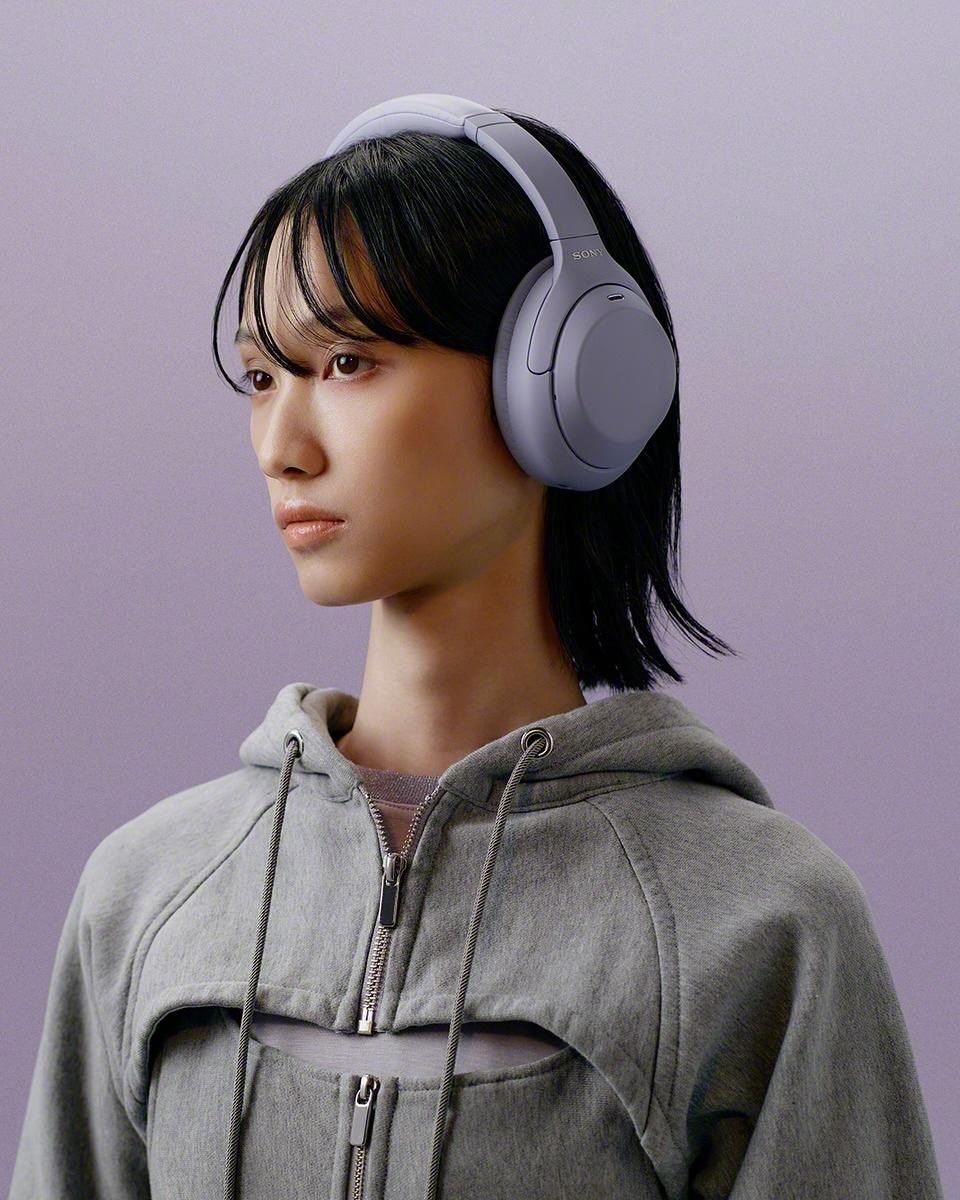 A person in a gray sweatshirt wearing lavender Sony WH-1000XM4C headphones.