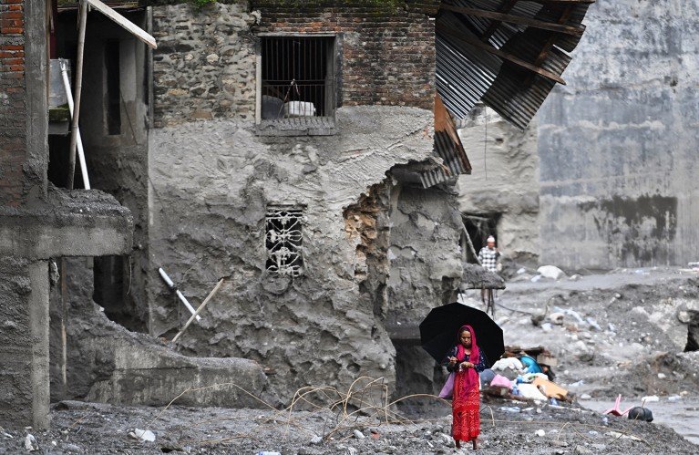 A woman wearing a red sari walks among the ruins of flash floods.