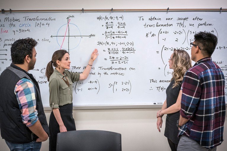 Mathematics university students discussing equations written on a whiteboard.