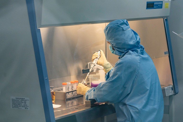A lab technician wearing PPE, working in a fume hood in a Chinese laboratory developing CAR-T cell therapies.
