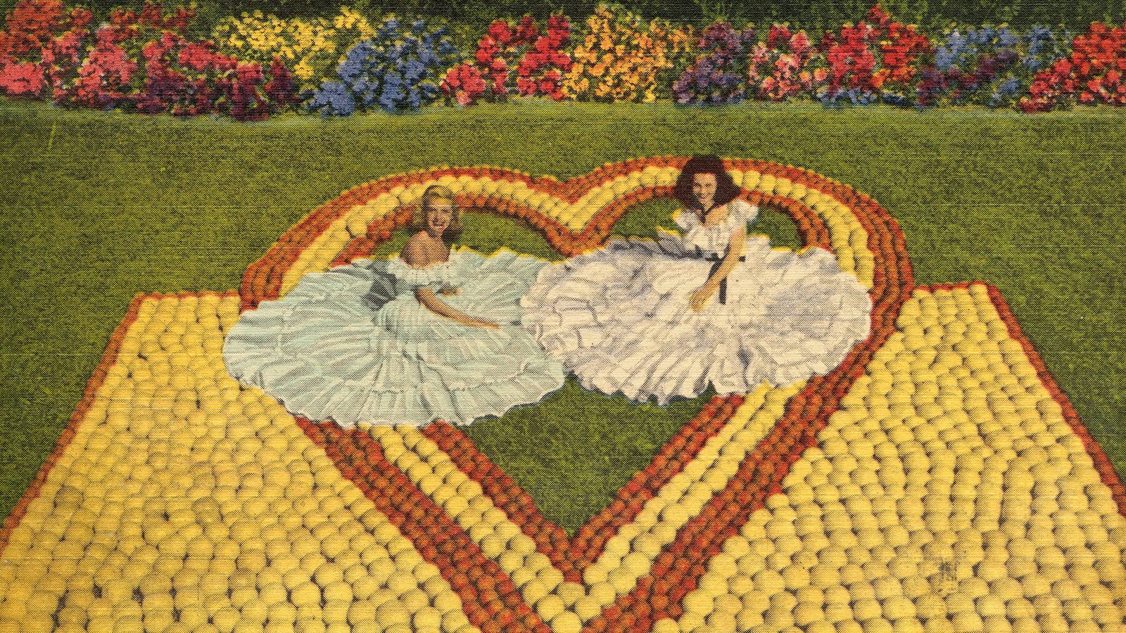 two women in big dresses pose wth the oranges and grapefruit in the shape of a heart.