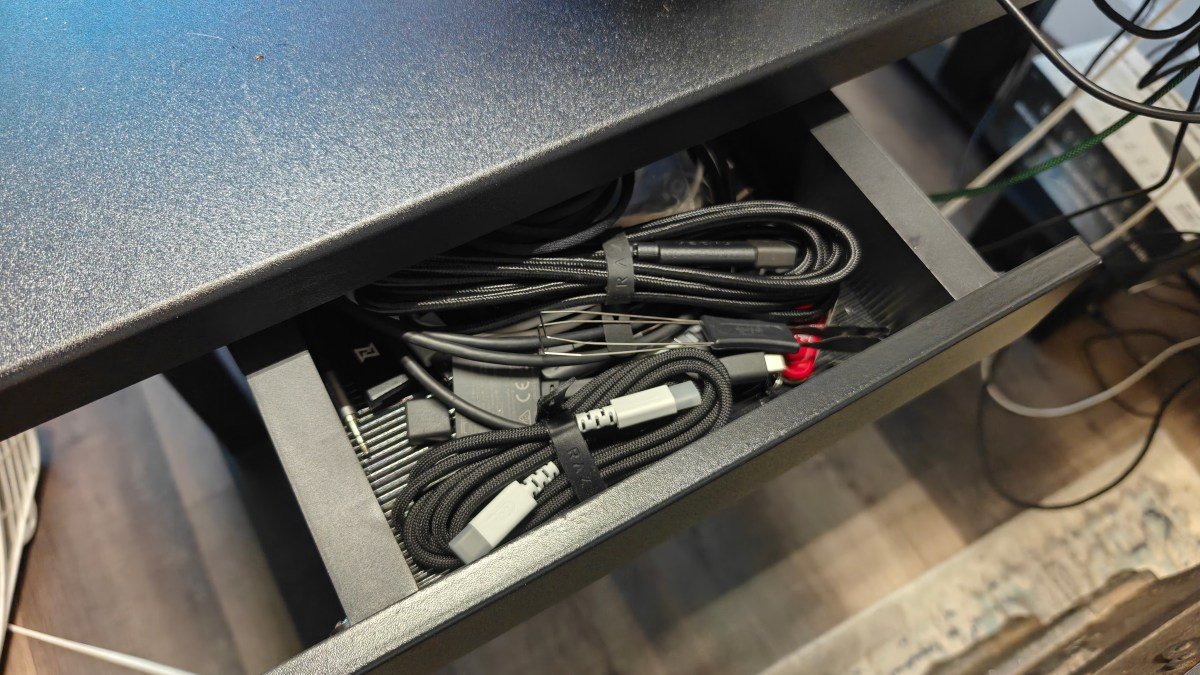 Open drawer on the MagVida standing desk with cables and computer accessories in side against a wood floor.