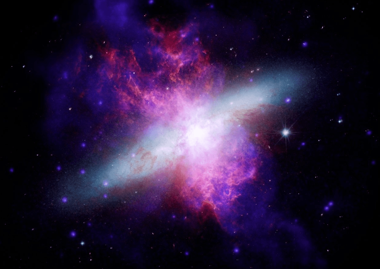 An irregular galaxy undergoing intense star formation because of a gravitational interaction with a neighboring galaxy hundreds of millions of years ago. Chandra X-rays (blue), supplemented by NuSTAR data, show towering superwinds of million-degree gas blowing thousands of light-years out of the galactic disk, with Hubble optical light (yellow, orange and white) showing the galaxy shape, and Webb and Spitzer detailing infrared dust emission (red). M82 was nicknamed the Cigar Galaxy mostly because of its edge-on angle to Earth, which makes its central disk look like an elongated, cigar-shaped oval with small optical telescopes. The galaxy illustrates how violent galactic "exhaust systems" can regulate a galaxy's growth by venting gas outwards. Image: X-ray: NASA/CXC/SAO; Optical: NASA/ESA/STScI; Infrared: NASA/ESA/CSA/STScI; Image Processing: NASA/CXC/SAO/L. Frattare, J. Major, and K. Arcand.