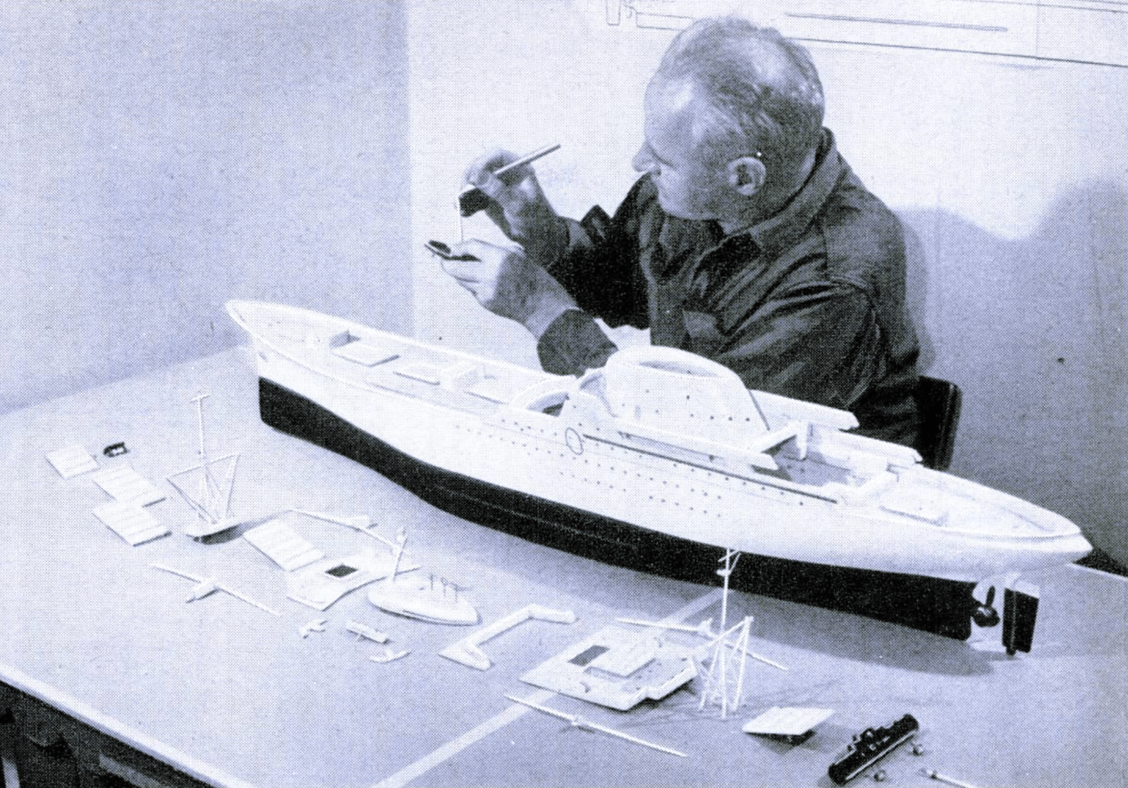 Black and white image of a white man assembling a ship model.
