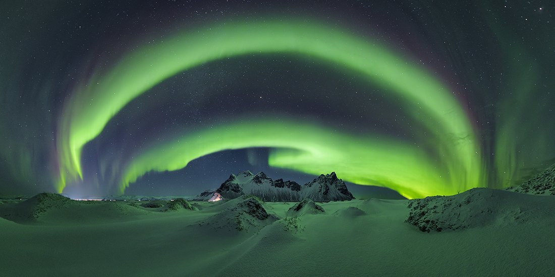 green aurora swirling above snow-covered mountains and landscape