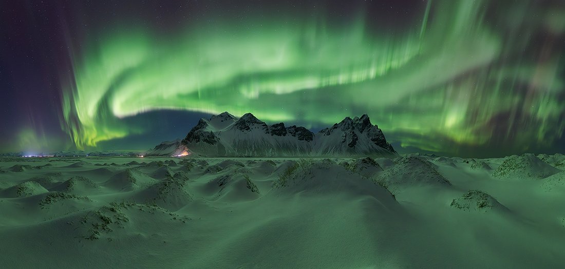 green aurora swirling above snow-covered mountains