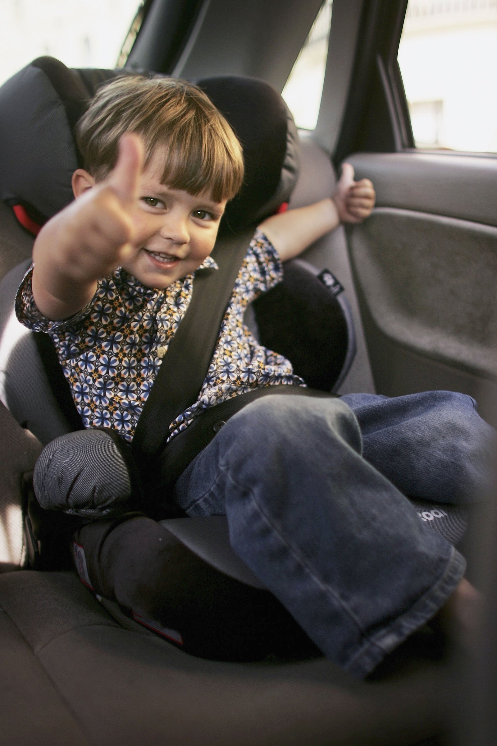 Toddler gives thumbs up from car seat.