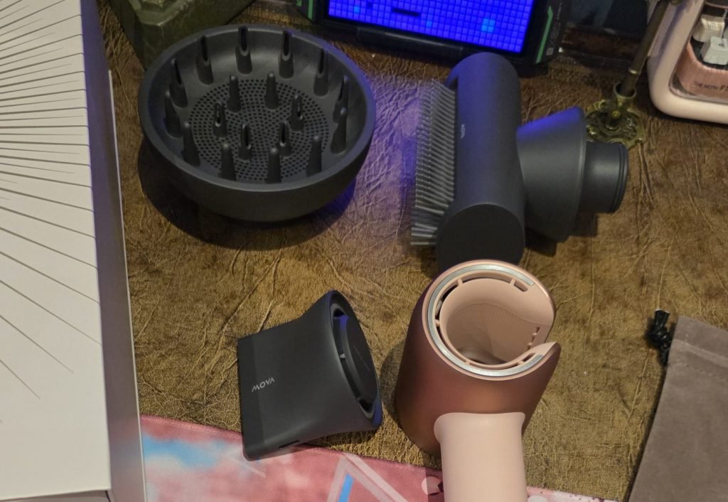 Hairdryer with three attachments, a half cone, a diffuser, and what looks like a wire brush. The hairdryer is facing up and the magnetic ring around the top of the hairdryer is facing the camera.