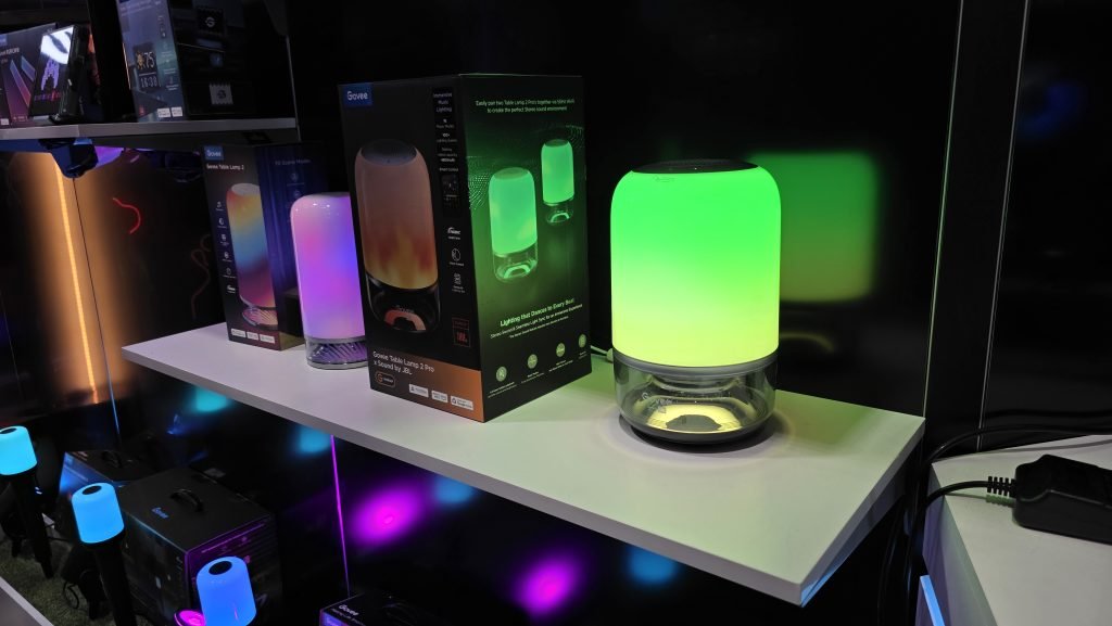 The Govee Lamp 2 Pro on the table in a mostly green colour, another next to it is lit up purpley-pink. The lamps have am elgongated-dome like look to them.