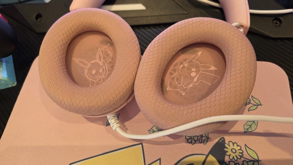 The headset is turned outward so you can see the inside of each earcup. On the left side is a pink on pink outline of Eevee, and on the right is a pink on pink outline of Pikachu.