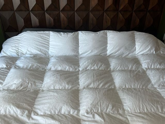 Brooklinen Comforter, a white blanket, on a bed with brown wooden headboard.