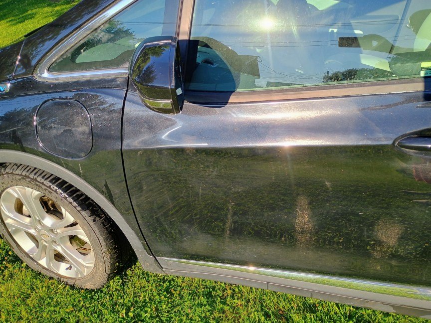 A black driver-side door after being washed with a power washer. A few mud splotches are still visible, and the tire is still fairly muddy.