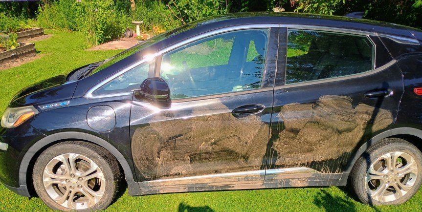 A black sedan with mud smeared on the driver-side tires and doors.