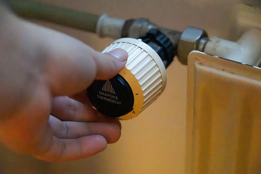 Man reaches for and turns a thermostat on a radiator.