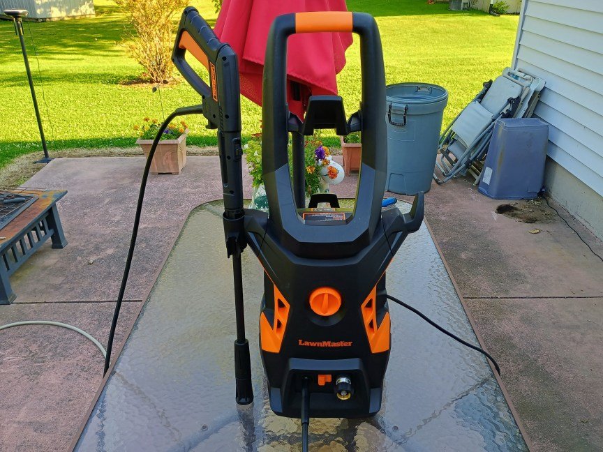 A black and orange LawnMaster LT506-2000A power washer sits fully assembled on a glass tabletop on a patio.