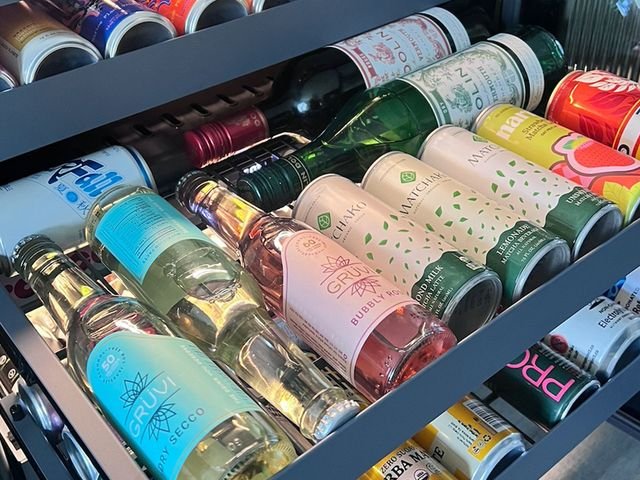 A small fridge with the door open and 2 bottom shelves slid out to show the bottles and cans within