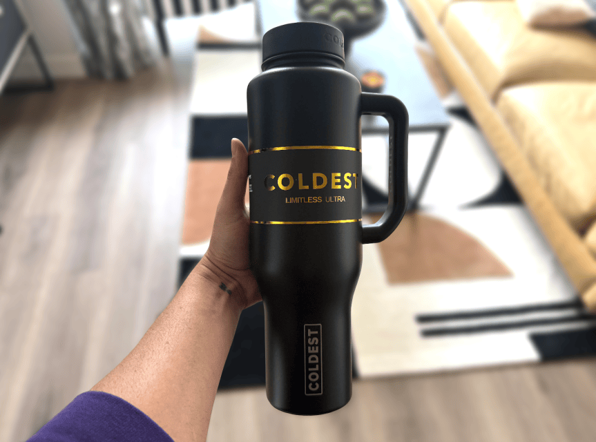 Person holds Coldest-brand water bottle featured in black with gold accents and lettering.